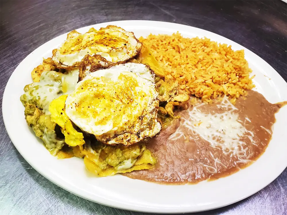 A plate of food on a black table, featuring fried eggs, brown sauce, fried rice, and fried chicken.