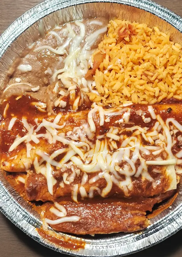 A colorful burrito on a silver tray, topped with shredded cheese, served with fluffy yellow rice and melted cheese.