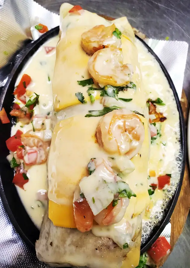 A seafood platter on a black plate, garnished with fresh tomatoes and herbs, served in a black cast iron skillet.