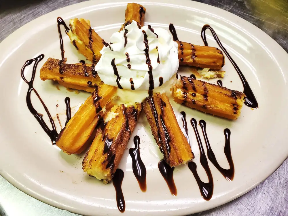 Golden brown pastries arranged in a star shape on a white plate with whipped cream and dark chocolate sauce drizzled on top.