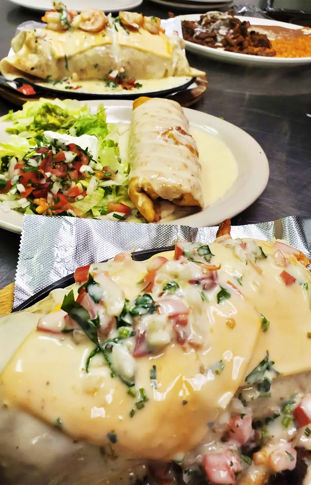 A table set with vibrant Mexican dishes, including tacos, burritos, salad, and meat, on a white tablecloth with colorful garnishes.