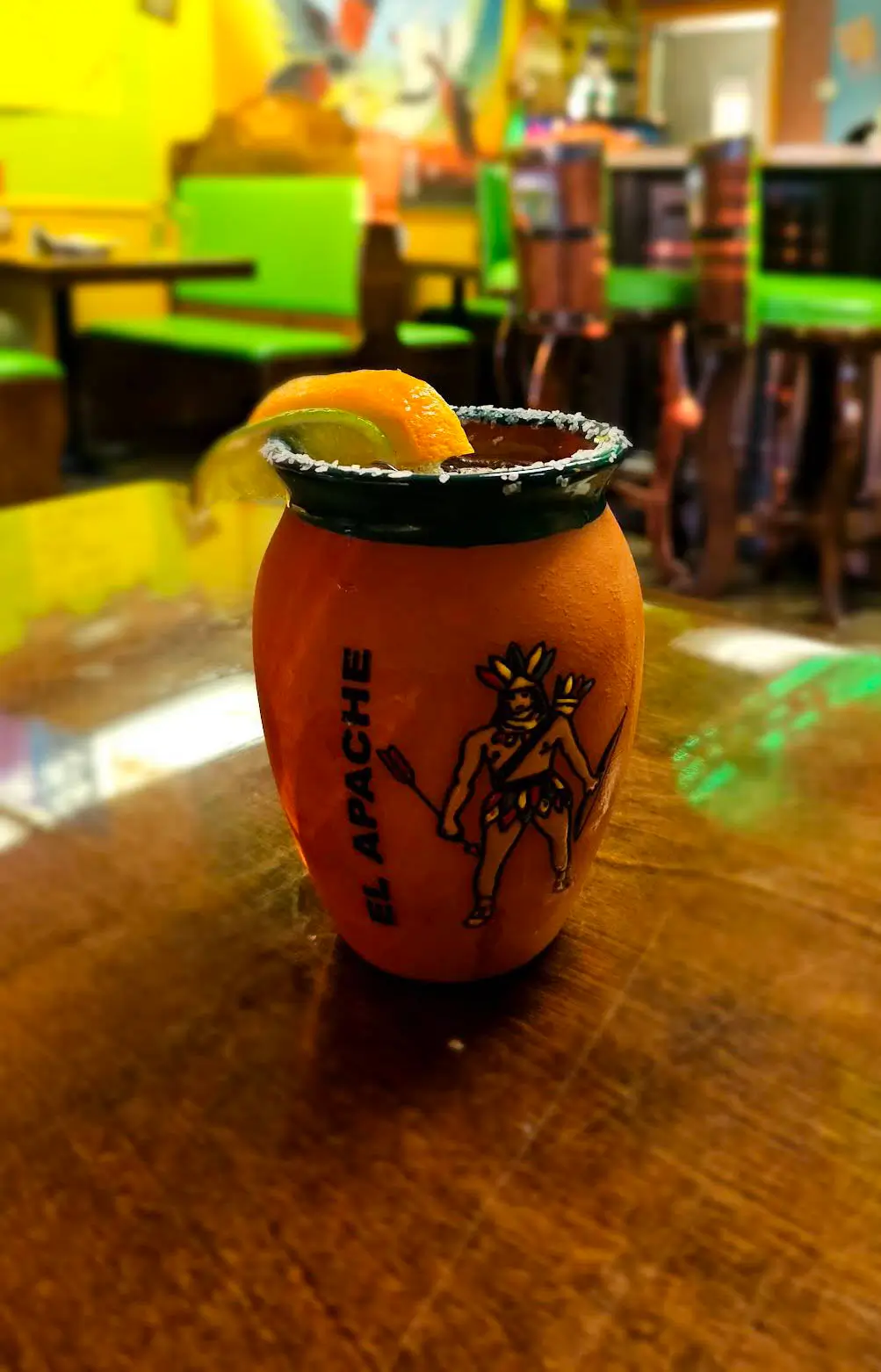 A small cup of margarita sits on a table, showcasing its vibrant color and garnished with a lime wedge.